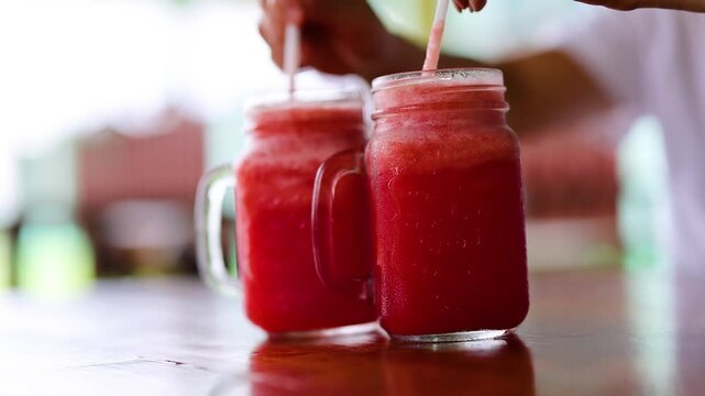 Close up of refreshing watermelon juice in mason jars with straws being picked up.