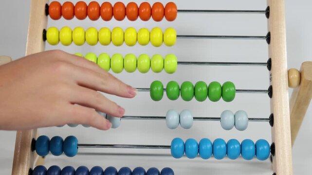 Close up of female hand using colorful wooden abacus toy to learn math and counting with sliding beads on white background.