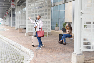 Diverse women waiting under canopy curbside  Senior African American woman waving phone, copy space © wavebreak3