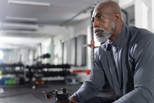 Senior African American man sitting at gym holding black shaker, wearing dark grey, copy space