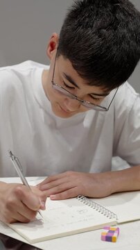 Close up of male person hand writing notes in notebook while studying. Real people, authentic learning, education and focus concept. Vertical video.