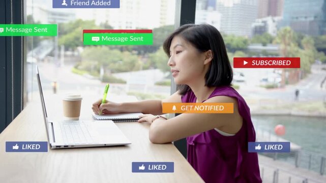 Woman writing at counter, laptop sending social alerts stacking around head, managing engagement