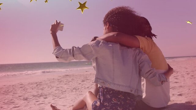 Two adults sitting on sand holding phone lifting selfie capturing travel shot drifting star overlay