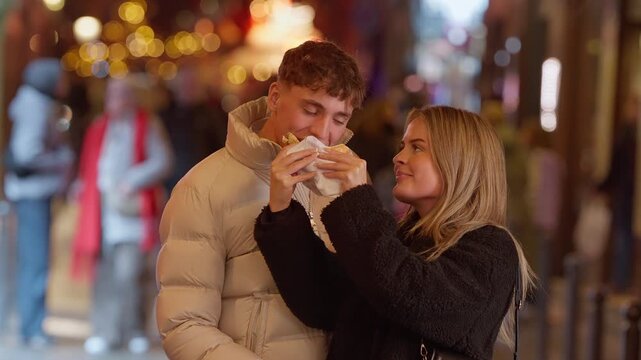 A romantic couple shares food on a street in Paris France at night The woman feeds the man a snack Bokeh lights are visible in the background The scene conveys love and travel.