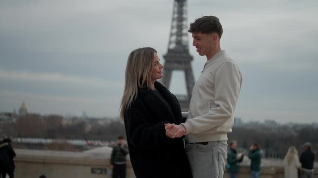 A romantic couple is holding hands in Paris France with the Eiffel Tower in the background The young lovers are embracing in front of the Parisian cityscape on an overcast.