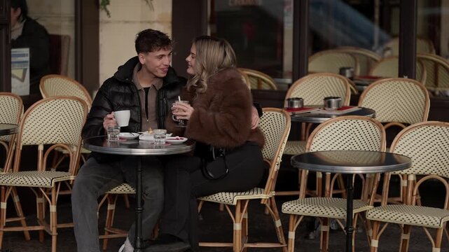 A young couple is sitting at an outdoor in Paris France They are drinking coffee talking and laughing The scene captures a romantic date in a classic French setting The man and woman appear to be enjo