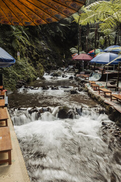 View of Grojogan Sewu Loket 2 featuring a cascading river surrounded by lush tropical ferns and colorful umbrellas over seating areas in Kecamatan Tawangmangu, Jawa Tengah, Indonesia.