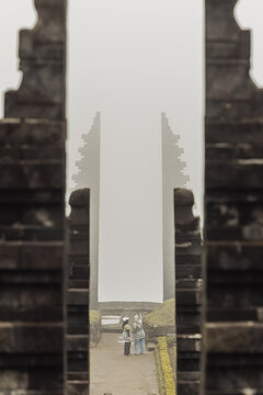View of Cetho Temple with two people standing between the iconic split stone gates under a misty sky in Kecamatan Jenawi, Jawa Tengah, Indonesia.