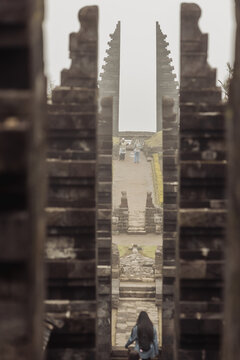 View of the historic Cetho Temple with its iconic split stone gateways and people walking along the path under a misty sky in Kecamatan Jenawi, Jawa Tengah, Indonesia.