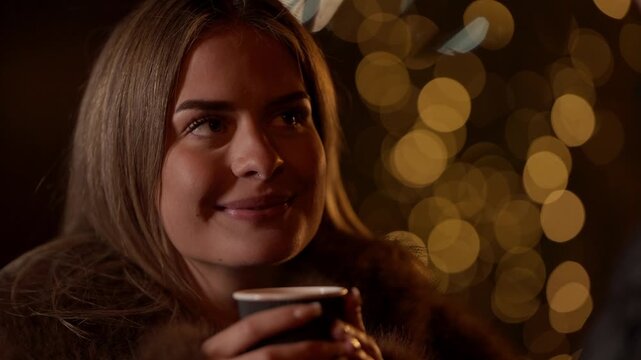 Close-up of a smiling woman holding a cup of coffee and talking to her partner in Paris at night The scene is romantic with bokeh lights in the background capturing a winter moment of love and connect