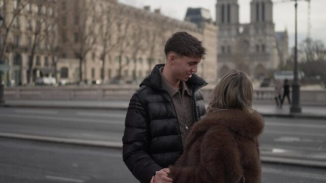 A romantic couple embraces on a bridge in Paris France with the Notre Dame Cathedral visible in the background The handheld shot captures the affection between the man and woman as they enjoy their ti