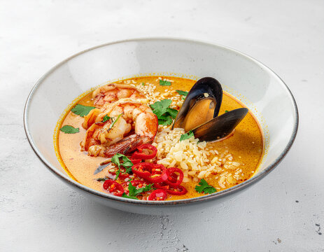 A vibrant bowl of Thai seafood curry featuring succulent shrimp, fresh mussels, and rice in a spicy coconut broth garnished with red chilies and cilantro.