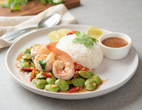 Fresh prawns stir-fried with stink beans (petai) and chili, served with a side of steamed rice, lime, and spicy dipping sauce on a minimalist plate.