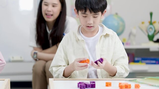 Asian Elementary Student Counting Math Blocks with Teacher in Bright Classroom