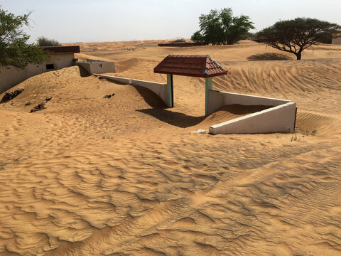 View of abandoned buildings and a small gate with a red roof partially buried by shifting desert sand dunes in Dubai, Dubai, United Arab Emirates.