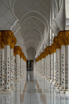 View of the ornate colonnade featuring white marble columns with floral inlays and golden palm capitals under pointed arches in Abu Dhabi, Abu Dhabi, United Arab Emirates.