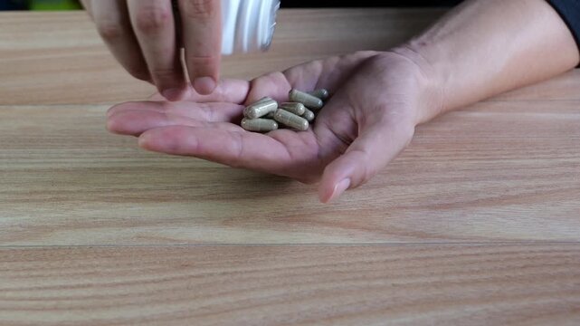 Close-up footage of green herbal capsules being poured from a plastic bottle into an open hand. Perfect for natural medicine, herbal supplement, alternative therapy, and wellness concepts.