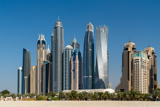 View of the modern Dubai Marina skyline featuring the twisted Cayan Tower and high-rise skyscrapers under a clear blue sky from the beach in Dubai, Dubai, United Arab Emirates.
