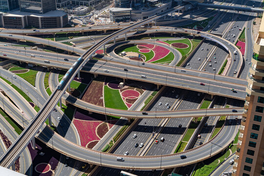 View of a complex multi-level highway interchange with a metro train on tracks and landscaped flower beds in Dubai, Dubai, United Arab Emirates.