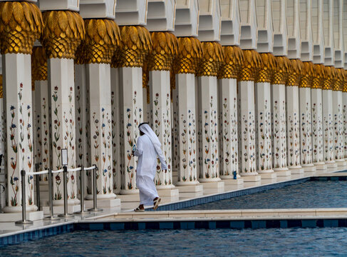 View of ornate white marble columns with gold leaf capitals and floral mosaics reflecting in a pool at the grand mosque in Dubai, Dubai, United Arab Emirates.