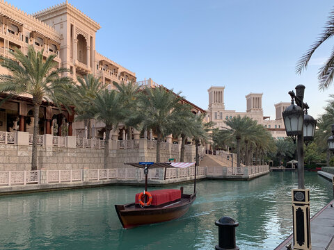 View of Madinat Jumeirah featuring a traditional abra boat on a canal surrounded by palm trees and wind towers under a clear sky in Dubai, Dubai, United Arab Emirates.