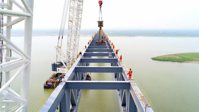 Workers on bridge structure assembly with crane lifting component