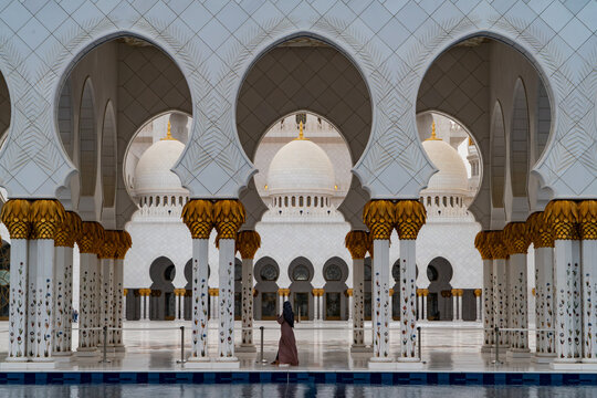 View of the Sheikh Zayed Grand Mosque featuring ornate white arches and floral columns with a person walking in the courtyard in Abu Dhabi, Abu Dhabi, United Arab Emirates.