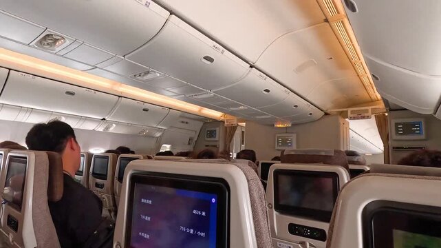 Passengers inside an airplane during flight traveling on a large commercial aircraft, view from the back seat of passenger.