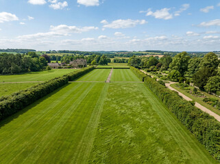 Naklejka premium Expansive green lawn, a meticulously manicured garden landscape with long hedges, perfect for elegant outdoor events and stately home backdrops. Lush grass field for luxury property and estate