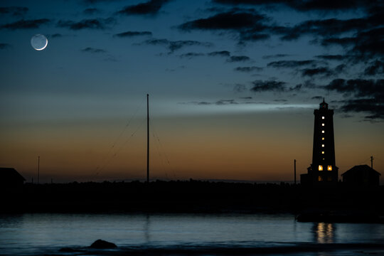 View of Grotta Lighthouse silhouetted against a twilight sky with a crescent moon and dark clouds over the water in Seltjarnarnes, Seltjarnarnesbaer, Iceland.