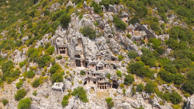Demre, Turkey. Dramatic facade of ancient Lycian rock-cut tombs carved into cliff face, close up aerial drone shot in bright summer daylight. Aerial View