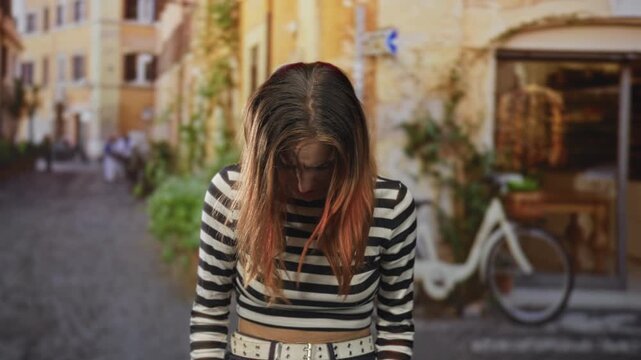 Woman with red hair, hair falling over her face, head bowed beside a bicycle on a cobblestone street; sadness solitude introspection.