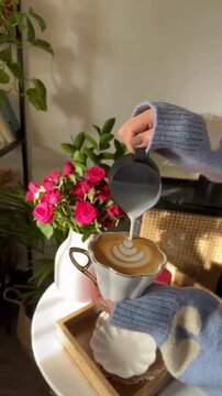 Pouring Creamer Milk into Coffee Cup Creating Aesthetic Swirl with Beautiful Red Flower Background, Cozy Cafe Drink Concept