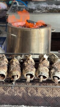 Vertical 4K shot of a whole salt-crusted grilled fish with a stake in its mouth being cooked on a hot charcoal grill.