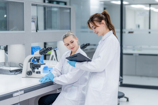 Two scientists work together in a modern lab discussing results while using a tablet in front of a microscope