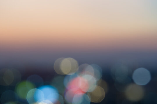 Abstract bokeh lights of city skyline at dusk with warm sunset background. Ideal for creative urban backdrops and festive designs.