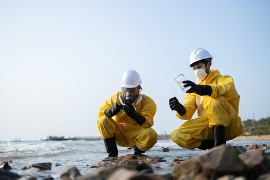 Scientist team in yellow protective suit conduct research on beach. specialist holds water sample for analysis, investigating environmental pollution and contamination