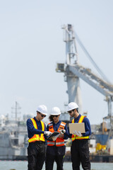 Fototapeta premium Team of diverse engineers and workers in hard hats and safety vests stand at port for serious discussion. They collaborate on planning for construction industry
