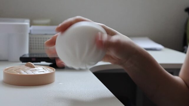 Close up video of female hands holding, squeezing and playing with a soft steamed bun shaped squishy toy indoors. Sensory relaxation, anti stress activity, anxiety relief