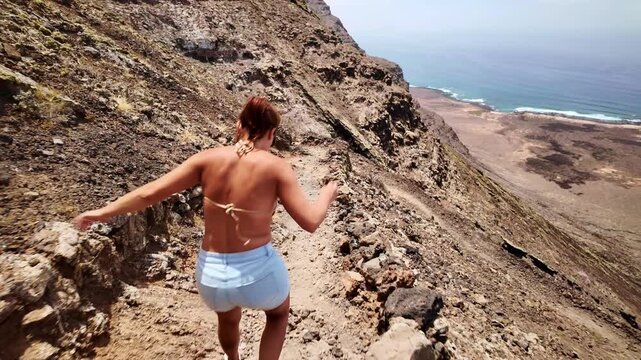 Adventurous woman trekking down a cliff path to Risco beach in Lanzarote