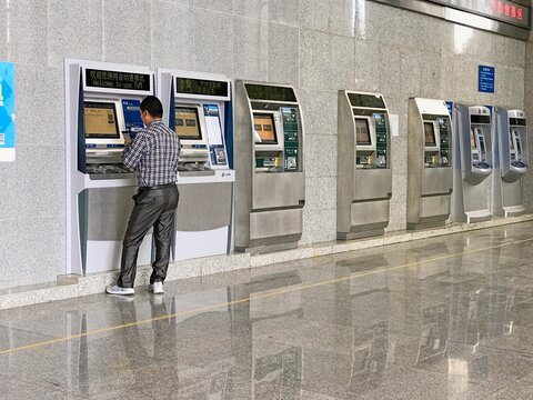 LIJIANG, CHINA - OCTOBER 25, 2017: A man using a CRH self-service ticket vending machine (TVM) inside a railway station in Lijiang, Yunnan province, featuring modern digital kiosks.