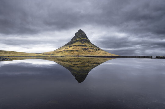 View of Kirkjufell mountain perfectly reflected in the calm surface of a lake under a dramatic overcast sky Kirkjufell, Grundarfjardarbaer, Iceland.