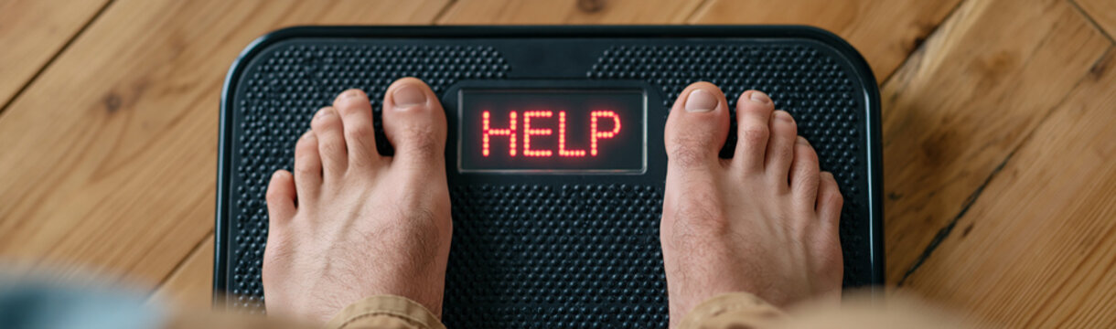 Weighing the Struggle: A stark close-up of bare feet standing on a weight scale, its digital display flashing the word HELP, embodying the struggles with health and weight management.