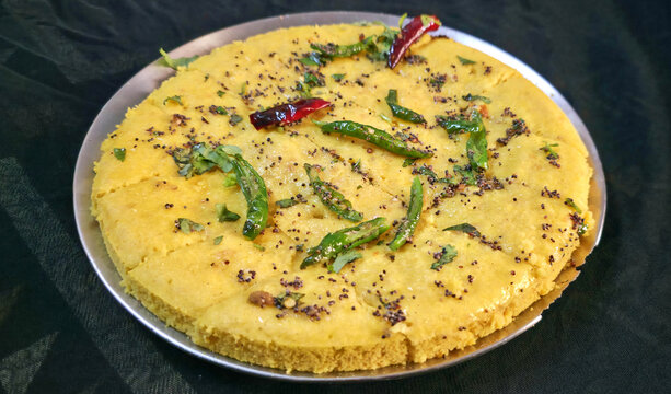 Fluffy yellow dhokla topped with mustard seeds, green chilies, and fresh coriander leaves.