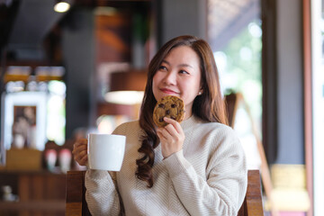 Portrait image of a woman eating a piece of chocolate chip cookie and drinking coffee in cafe © Farknot Architect
