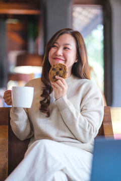 Vertical portrait image of a woman eating a piece of chocolate chip cookie and drinking coffee in cafe