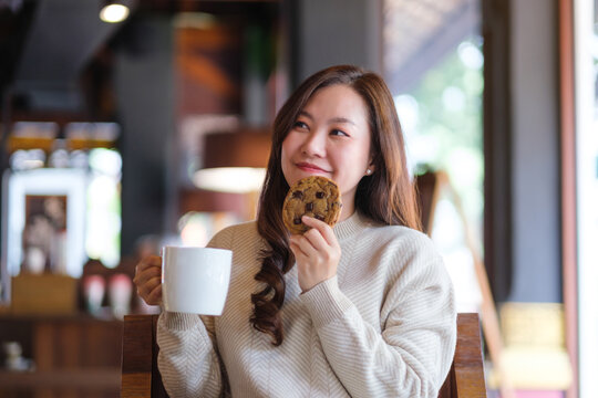 Portrait image of a woman eating a piece of chocolate chip cookie and drinking coffee in cafe