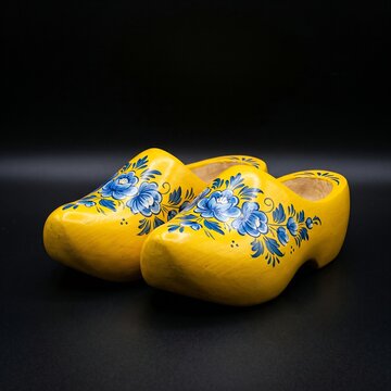 Traditional Dutch Wooden Clogs (Klompen): A pair of classic yellow-painted Dutch wooden clogs with hand-painted blue floral motifs, placed side-by-side, studio lighting, deep black background, 1:1 rat
