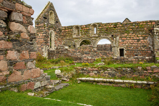 View of the ancient stone ruins of Iona Nunnery with pink granite walls and Romanesque arches under an overcast sky in Baile Mor, Scotland, United Kingdom.