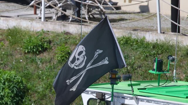 Pirate flag with skull and crossbones waving on boat roof in wind.